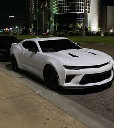 a white chevrolet camaro parked on the side of the road at night with buildings in the background