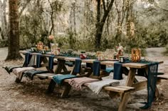 a picnic table set up in the woods with blue linens and napkins on it