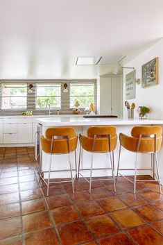 three yellow chairs are sitting at the bar in this modern kitchen with tile flooring