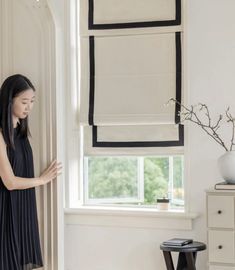 a woman standing in front of a window next to a vase with flowers on it