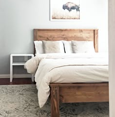 a bed with white linens and pillows in a small room next to a painting on the wall