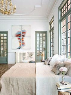 a large bed sitting in a bedroom under a chandelier next to two windows