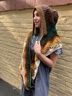 a woman standing in front of a brick wall wearing a multicolored crocheted scarf