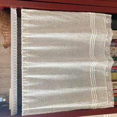 a shelf with some books on top of it and a white curtain hanging from the side