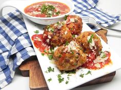 meatballs with sauce and parmesan cheese are on a plate next to a bowl of soup