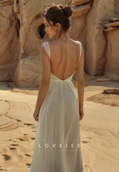 the back of a woman in a white dress standing on top of a sandy beach