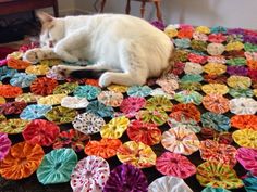 a white cat laying on top of a multicolored rug covered in paper flowers