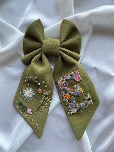 a green bow with flowers and beads on it is laying on a white cloth background