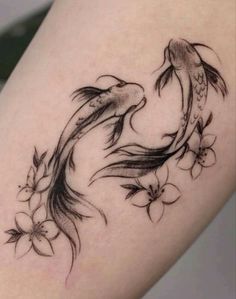 a woman's thigh with a tattoo of two koi fish and flowers on it