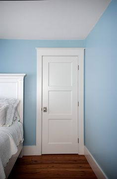 a white bed sitting next to a blue wall in a room with a wooden floor