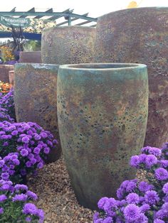 three large vases sitting next to each other in front of purple flowers and gravel