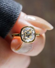 a woman's hand holding a ring with a white diamond in the middle and gold band