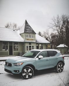 a light blue car parked in front of a building with snow on the ground and trees