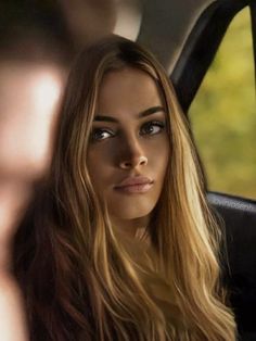 a woman sitting in the back seat of a car looking at her reflection on the mirror