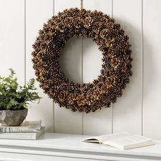 a wreath sitting on top of a white mantle next to a book and potted plant