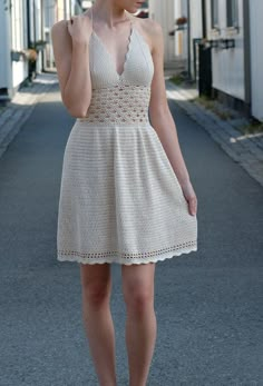 a woman in a white dress is walking down the street and talking on her cell phone