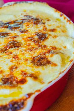 a red casserole dish sitting on top of a wooden table covered in cheese