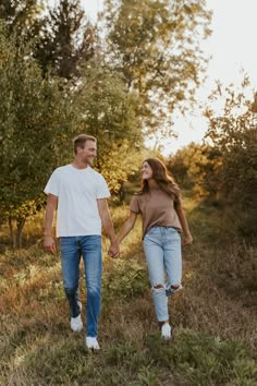 a man and woman holding hands while walking through the grass in an apple orchard at sunset