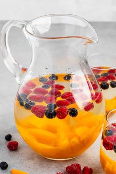 a pitcher filled with fruit and berries next to two glasses full of water on a table