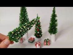 miniature christmas trees and presents are being held by a person's hand in front of them