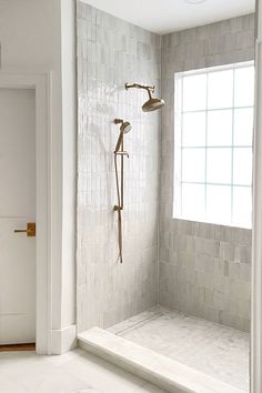 an empty bathroom with white tile and gold fixtures on the shower head, tub, and window