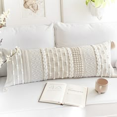 a white couch with a book, cup and vase on it next to an open book