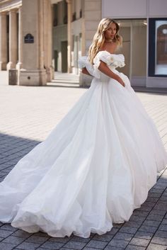 a woman in a white wedding dress is standing on the sidewalk and looking at the camera