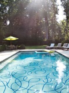 an empty swimming pool with lounge chairs and umbrellas in the back ground, surrounded by trees