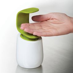 a person holding an object in their hand on top of a white table with a green lid