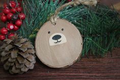 a wooden ornament with a bear's face on it next to pine cones and berries