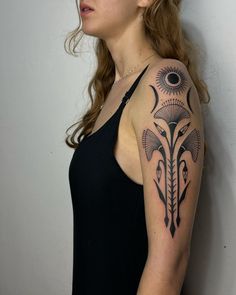 a woman with a black and grey tattoo on her arm, standing in front of a white wall