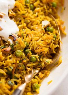 a spoon full of rice and peas with sour cream on top, in a white bowl