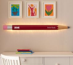 a red pencil sitting on top of a white desk next to two framed pictures and a chair