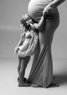 a black and white photo of a pregnant woman holding her daughter's hand over her belly