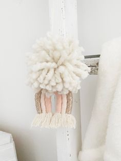 a white stuffed animal hanging from the side of a door with two pink and beige pom poms