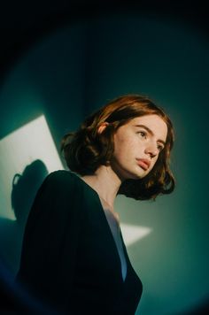 a woman standing in front of a wall with her head turned to the side and light shining on her face