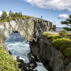 a man standing on top of a cliff next to the ocean with a bridge over it