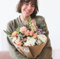 a woman is holding a bouquet of flowers in her arms and smiling at the camera