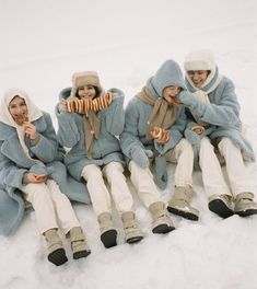 four people sitting in the snow eating hotdogs and wearing winter clothes with hoods