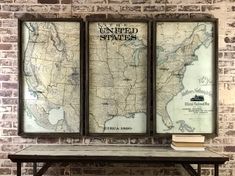 two framed maps sitting on top of a wooden table in front of a brick wall