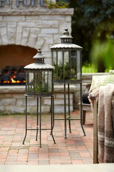 two metal lanterns sitting on top of a brick floor next to a fire place in front of a stone fireplace