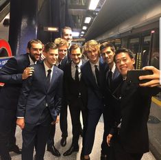 a group of men standing next to each other in front of a subway train at a station