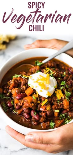 two hands holding a bowl of chili with sour cream