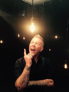 a man in black shirt holding his finger up with light bulbs on the ceiling behind him