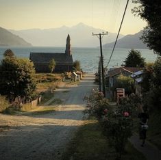 a person riding a bike down a dirt road next to the ocean with mountains in the background