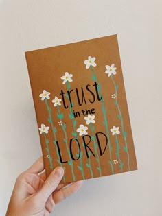 a hand holding up a card that says trust in the lord with daisies on it