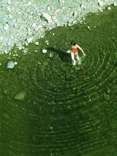 a person standing in the middle of a body of water surrounded by rocks and pebbles