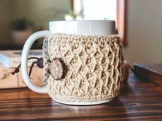 a crocheted coffee cup cozying up on a table next to a book