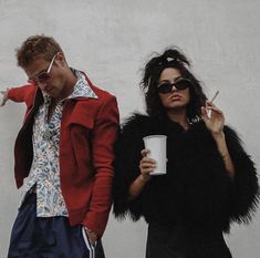 a man and woman standing next to each other holding coffee cups in front of a building