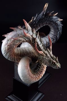 a statue of a dragon on a black pedestal with its tail curled up and it's eyes closed